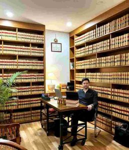 Raghav Chadha at a wooden desk in a law office surrounded by shelves filled with legal books, working on a laptop in a well-lit library setting.