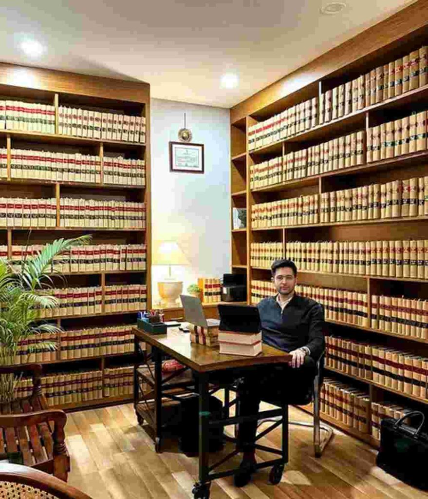 Raghav Chadha at a wooden desk in a law office surrounded by shelves filled with legal books, working on a laptop in a well-lit library setting.